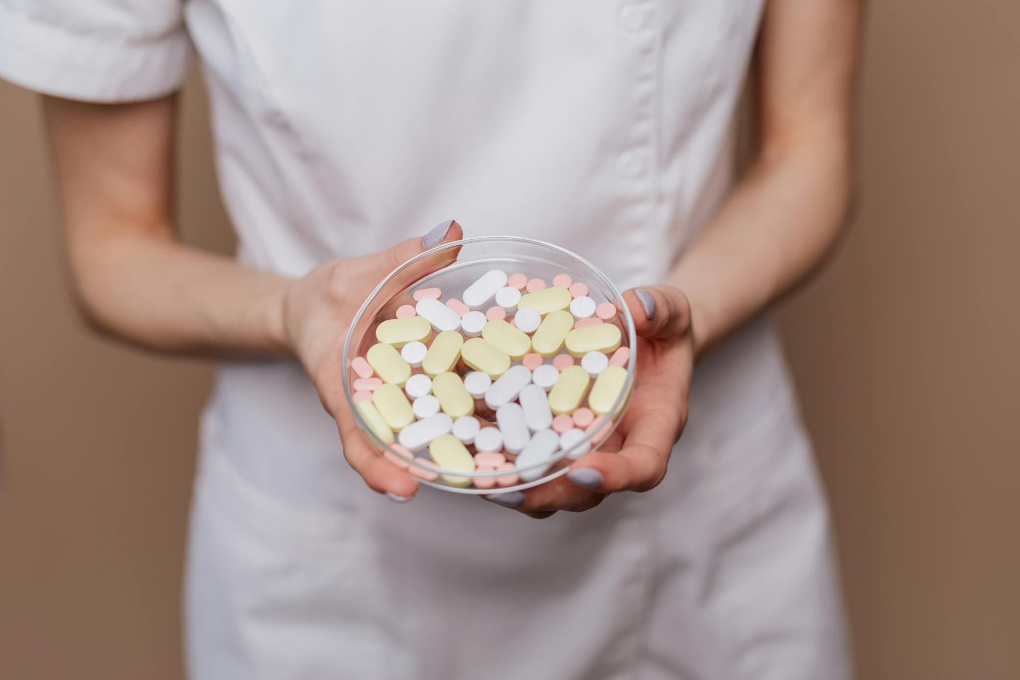 Close-up of a medical professional holding a petri dish filled with pills and tablets.
